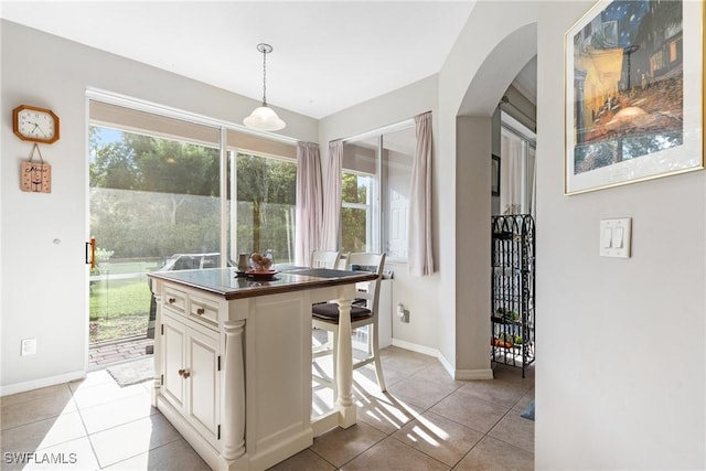 kitchen featuring pendant lighting, light tile patterned floors, dark countertops, white cabinets, and arched walkways