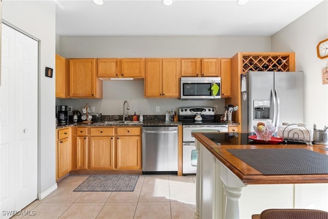 kitchen with dark stone countertops, a sink, stainless steel appliances, and light tile patterned floors