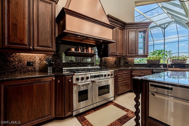 kitchen with dark brown cabinetry, light tile patterned floors, custom range hood, range with two ovens, and dark stone counters