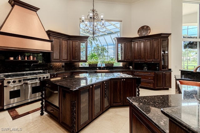 kitchen with dark brown cabinets, double oven range, a center island, dark stone countertops, and a notable chandelier