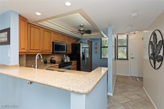 kitchen featuring light stone counters, kitchen peninsula, backsplash, appliances with stainless steel finishes, and ceiling fan