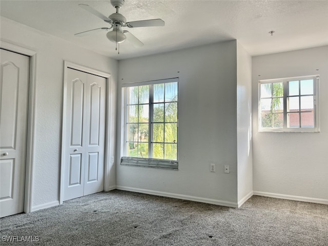 unfurnished bedroom with carpet, multiple windows, ceiling fan, and multiple closets