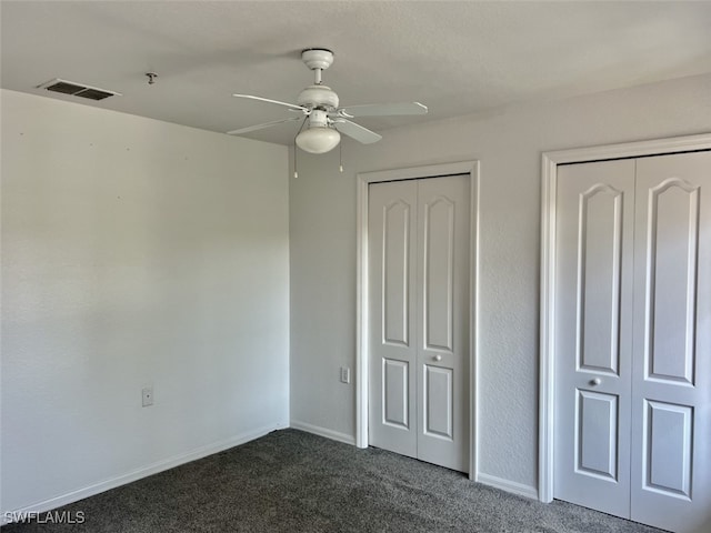 unfurnished bedroom with dark colored carpet, ceiling fan, and multiple closets