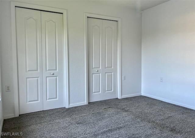 unfurnished bedroom with dark carpet and multiple closets