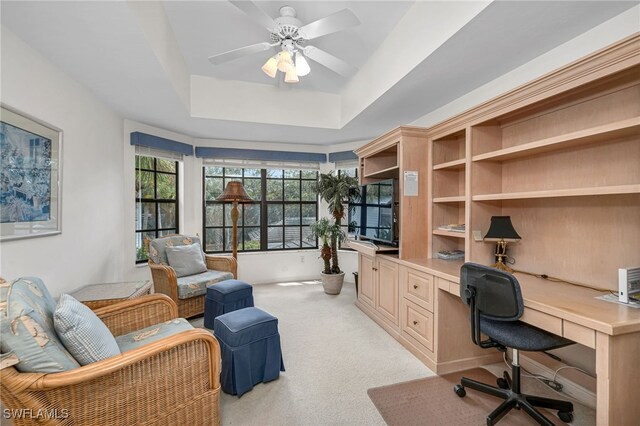 office area with light colored carpet, a tray ceiling, and ceiling fan