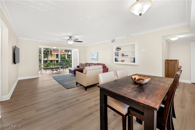 dining room with built in shelves, light wood-type flooring, ceiling fan, and ornamental molding