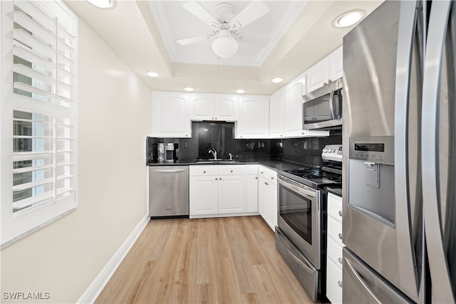 kitchen featuring sink, light hardwood / wood-style flooring, appliances with stainless steel finishes, a tray ceiling, and white cabinetry