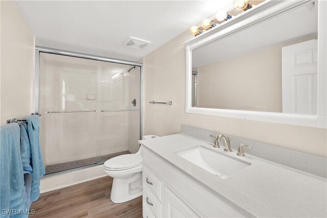 bathroom with hardwood / wood-style flooring, vanity, toilet, and a shower with shower door