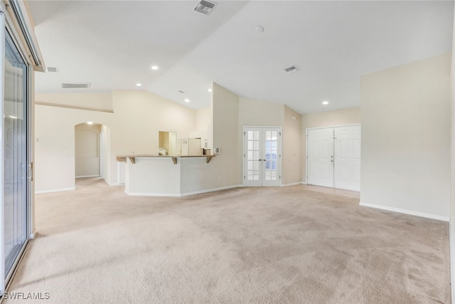 unfurnished living room with vaulted ceiling, light colored carpet, and french doors