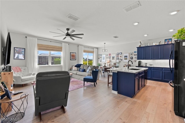 kitchen with light hardwood / wood-style floors, blue cabinetry, black refrigerator, ceiling fan, and a center island with sink