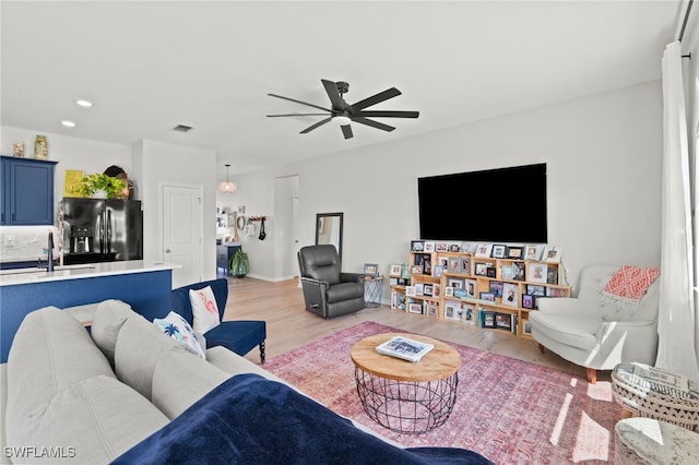 living room with light hardwood / wood-style floors, ceiling fan, and sink