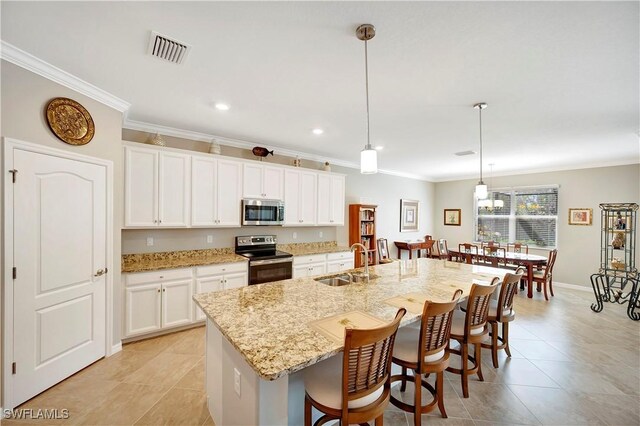 kitchen with an island with sink, white cabinets, stainless steel appliances, decorative light fixtures, and sink