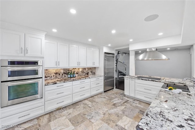 kitchen with wall chimney exhaust hood, white cabinetry, sink, and appliances with stainless steel finishes