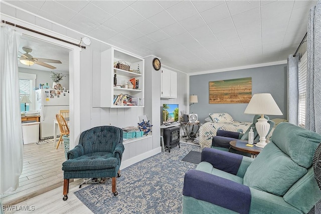 living room featuring wood-type flooring, built in features, ceiling fan, and ornamental molding