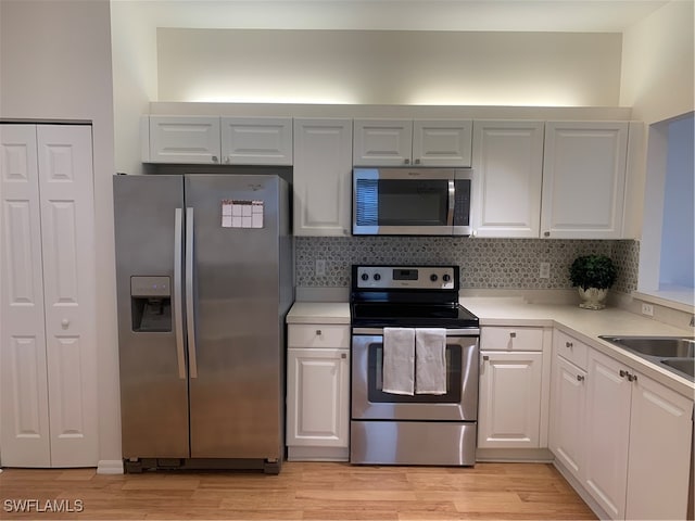 kitchen with sink, appliances with stainless steel finishes, backsplash, white cabinets, and light wood-type flooring