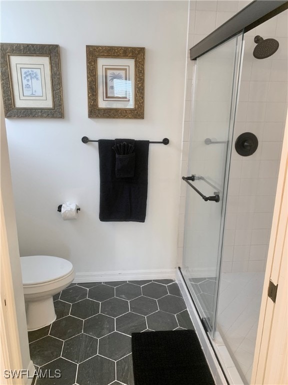 bathroom featuring tile patterned flooring, a shower with shower door, and toilet