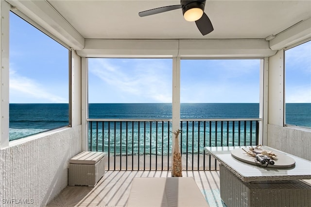 unfurnished sunroom featuring a water view, ceiling fan, and a beach view