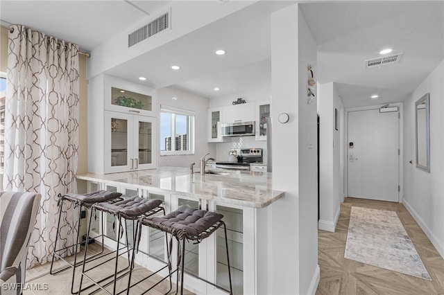 kitchen featuring appliances with stainless steel finishes, kitchen peninsula, a kitchen breakfast bar, white cabinets, and light stone counters