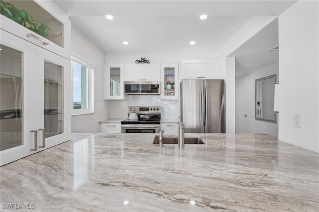 kitchen with appliances with stainless steel finishes, white cabinets, light stone countertops, and sink