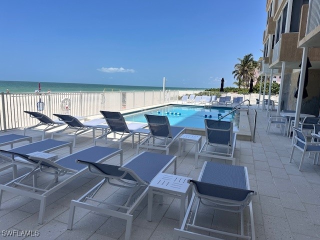 view of pool featuring a water view, a patio, and a beach view