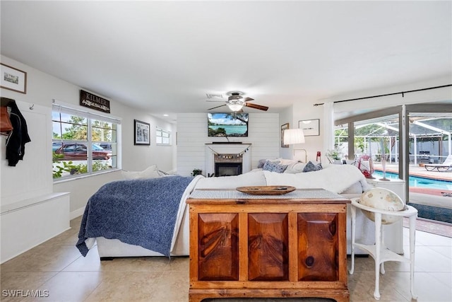 tiled bedroom featuring ceiling fan, access to outside, a brick fireplace, and multiple windows