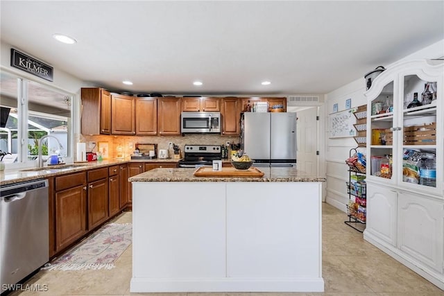 kitchen featuring stainless steel appliances, decorative backsplash, a kitchen island, light stone counters, and sink