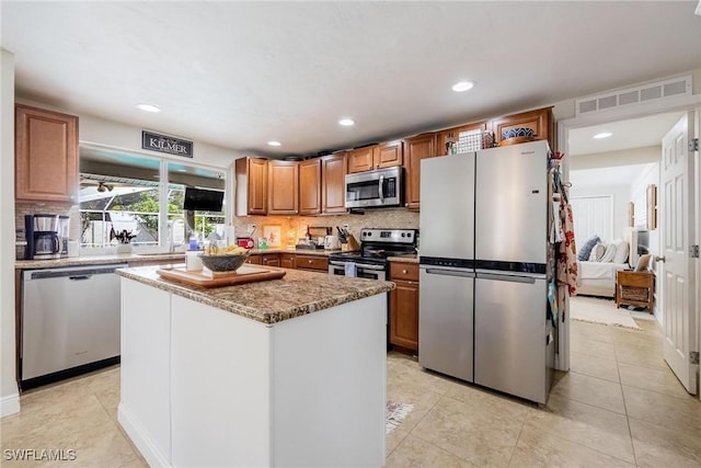 kitchen with light tile patterned floors, appliances with stainless steel finishes, backsplash, a kitchen island, and sink