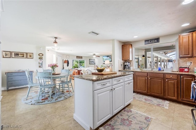 kitchen featuring ceiling fan, decorative backsplash, a center island, stone countertops, and sink