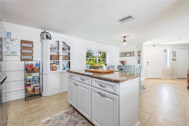 kitchen with light stone countertops, light tile patterned floors, white cabinets, and a kitchen island