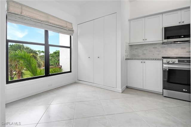 kitchen featuring light stone counters, light tile patterned floors, tasteful backsplash, white cabinetry, and stainless steel appliances