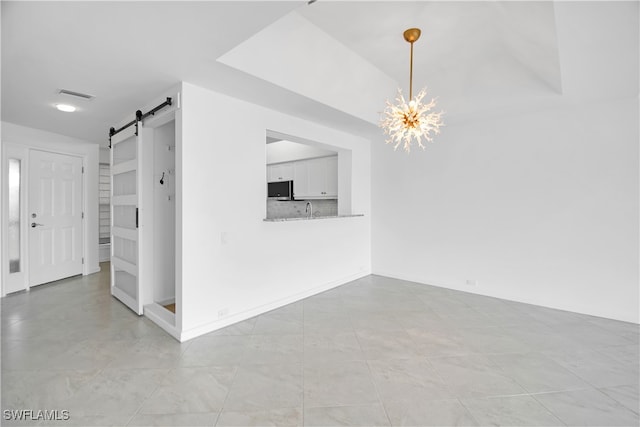 spare room featuring sink, a chandelier, and a barn door