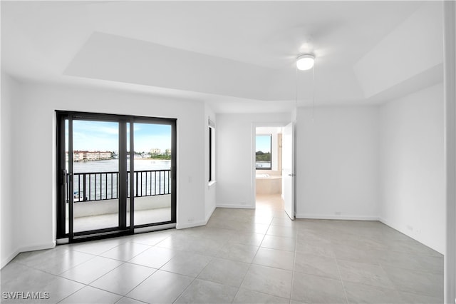 empty room featuring a raised ceiling, light tile patterned floors, and a water view