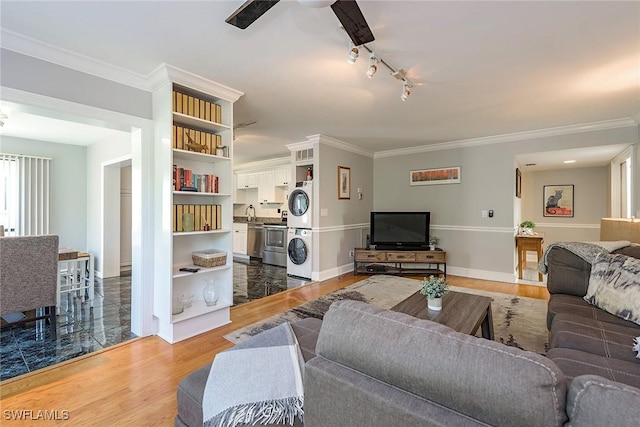 living room with track lighting, stacked washer / dryer, crown molding, and wood-type flooring