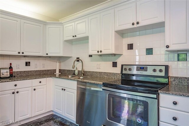 kitchen with decorative backsplash, white cabinetry, appliances with stainless steel finishes, dark stone countertops, and sink