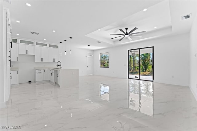 unfurnished living room featuring a tray ceiling, ceiling fan, and sink