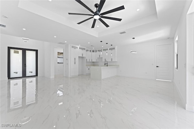 unfurnished living room featuring ceiling fan, french doors, sink, and a tray ceiling