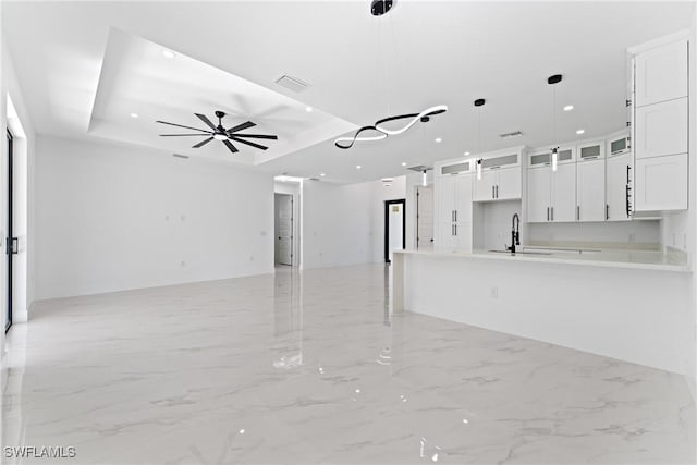 unfurnished living room featuring a raised ceiling, ceiling fan, and sink