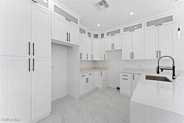 kitchen with white cabinetry, light stone counters, and sink