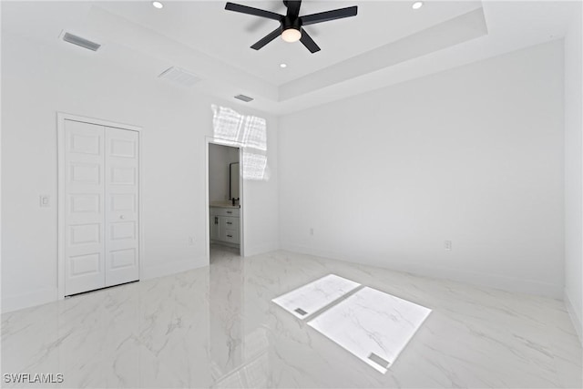 unfurnished bedroom with ceiling fan, ensuite bathroom, a tray ceiling, and a closet