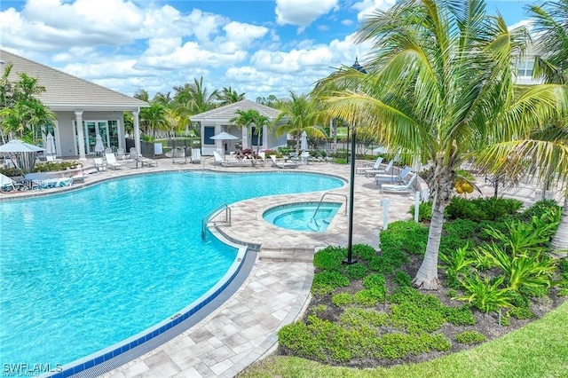 community pool with a patio area, fence, and a hot tub