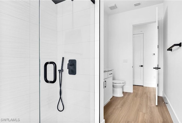 bathroom featuring wood finished floors, visible vents, toilet, and tiled shower