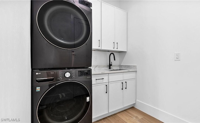 laundry area featuring light wood-style flooring, a sink, baseboards, stacked washer / drying machine, and cabinet space