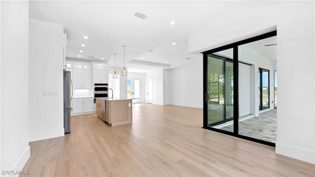 kitchen with light wood-style flooring, a kitchen island with sink, open floor plan, stainless steel appliances, and light countertops