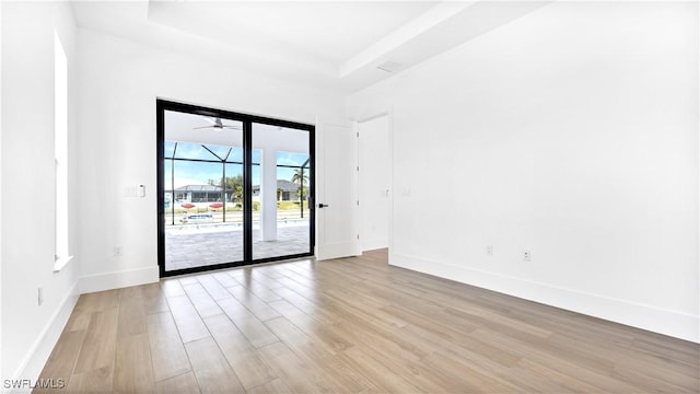 empty room with a raised ceiling, light wood-type flooring, and baseboards