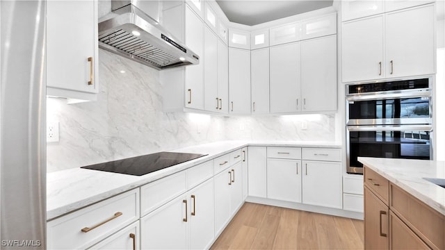 kitchen with stainless steel double oven, black electric stovetop, tasteful backsplash, and wall chimney exhaust hood