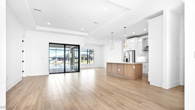 unfurnished living room with a raised ceiling, visible vents, light wood-style flooring, and baseboards