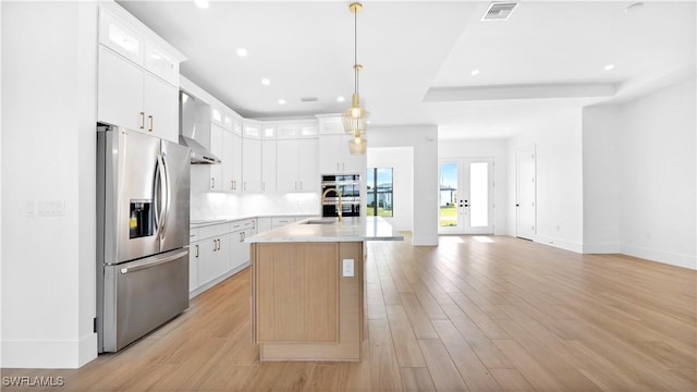 kitchen featuring visible vents, light wood-style flooring, stainless steel appliances, light countertops, and wall chimney range hood