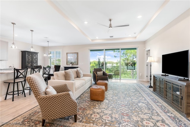 living room featuring ceiling fan with notable chandelier, light hardwood / wood-style flooring, and a raised ceiling