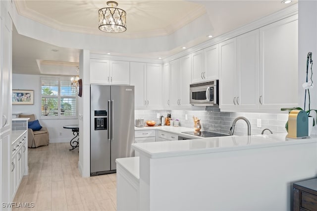 kitchen featuring stainless steel appliances, a raised ceiling, a chandelier, white cabinets, and ornamental molding