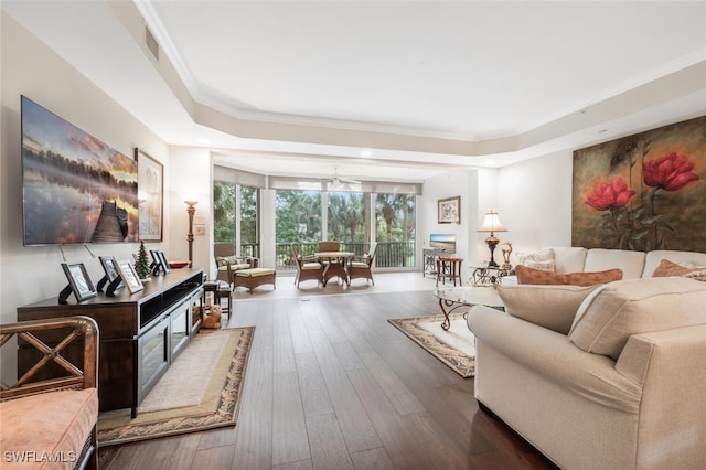 interior space featuring a tray ceiling, visible vents, crown molding, and wood finished floors